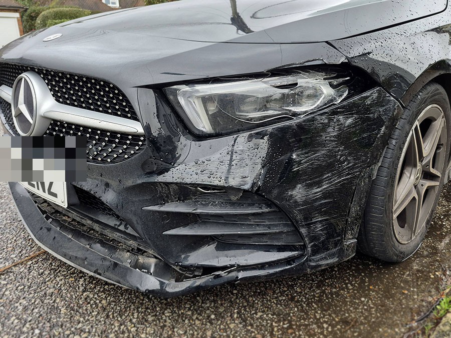 Cracked headlight and scuffed front bumper on a black Mercedes awaiting bumper repair