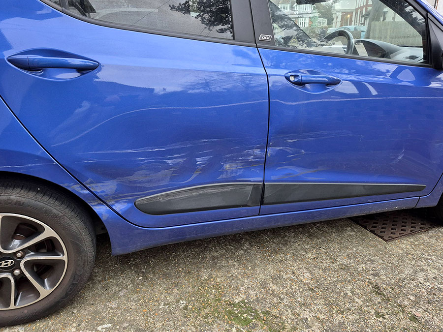 Crease dent along the door panel of a blue Hyundai needing panel repair